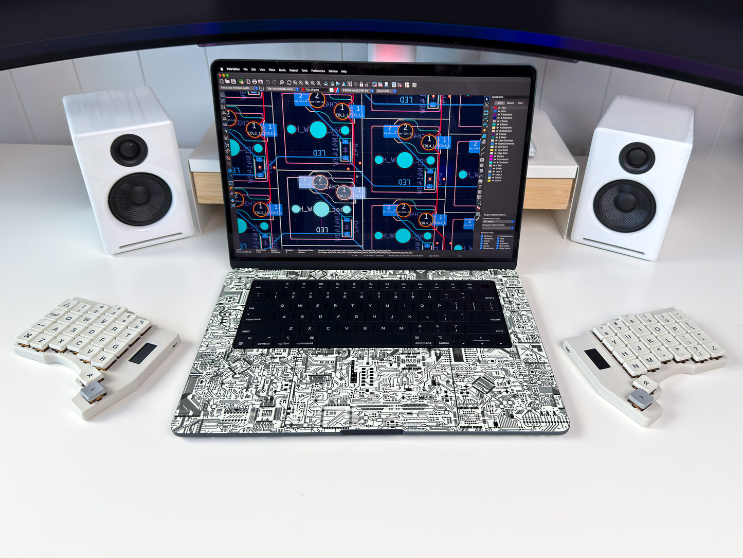 Laptop with a unique skin on a desk with speakers and a keyboard.